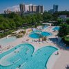 Veduta dall'alto di un parco acquatico con piscine, vegetazione e edifici in lontananza.